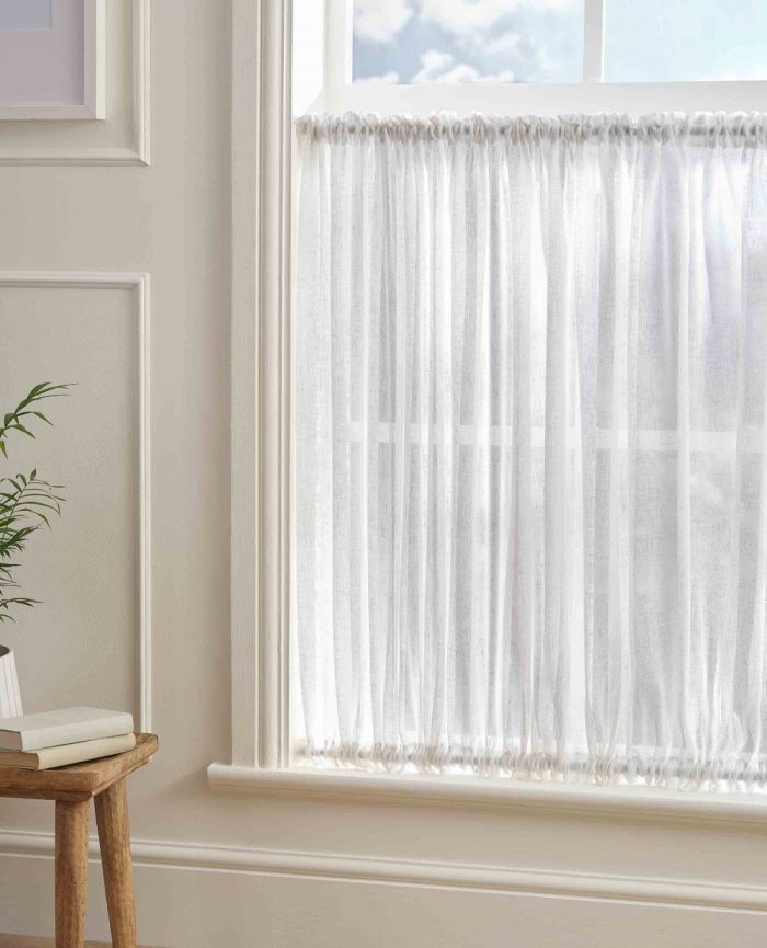 White cafe curtain hanging in front of a window with light flooding in