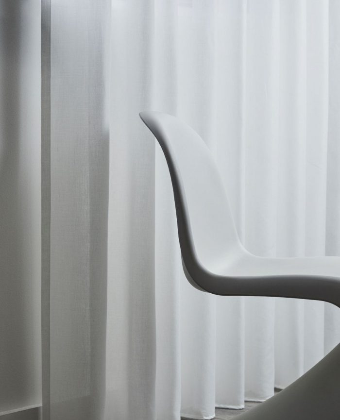 White flowy voile curtains hanging with a white chair in front
