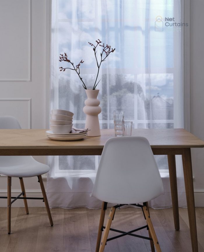 White voile curtain hanging on a window in a dining room with some table and chairs
