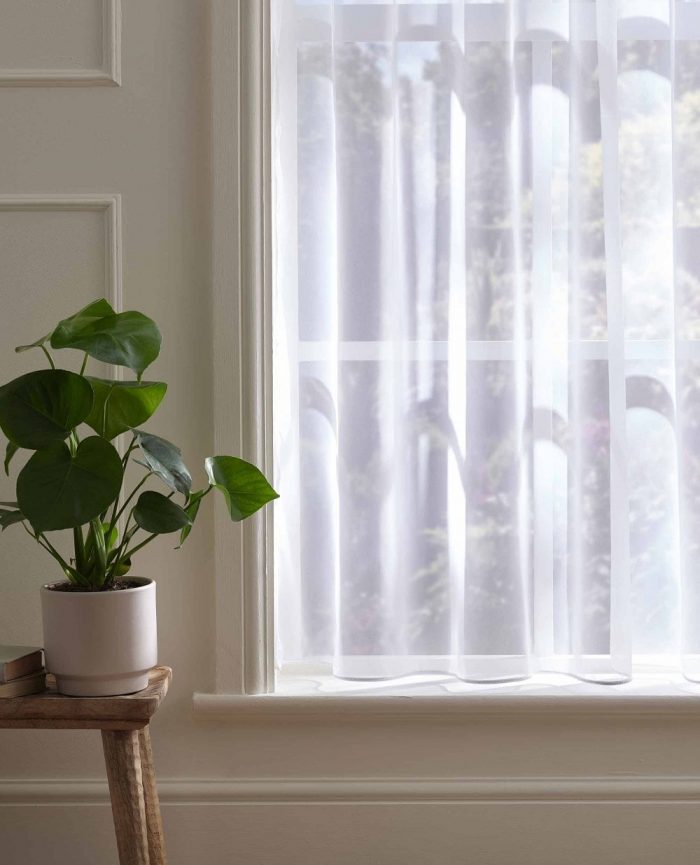 White voile curtain hanging on a window shining in the sun