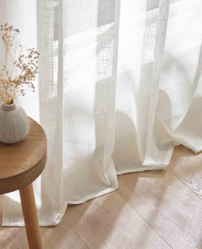 White linen curtain draping onto a wooden floor